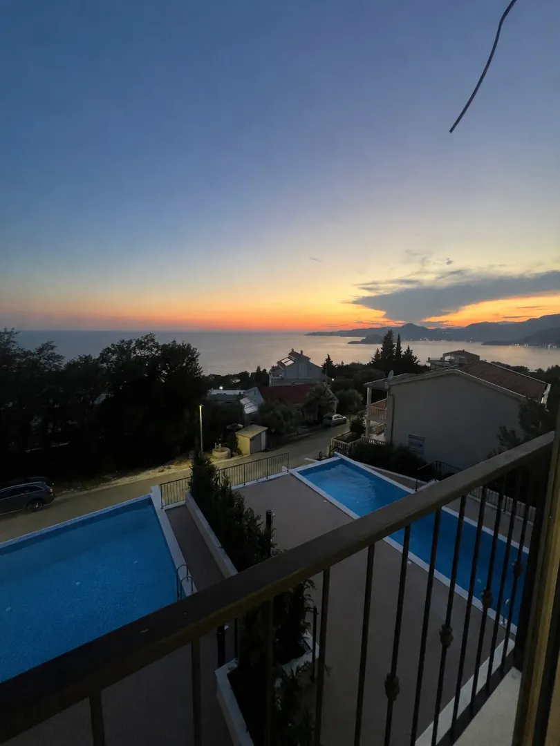 Pogled sa terase na bazene, okolno naselje i zalazak sunca iznad mora.