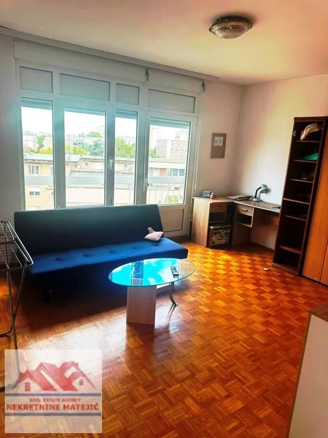 Living room with a blue sofa, wooden flooring, and a large window.