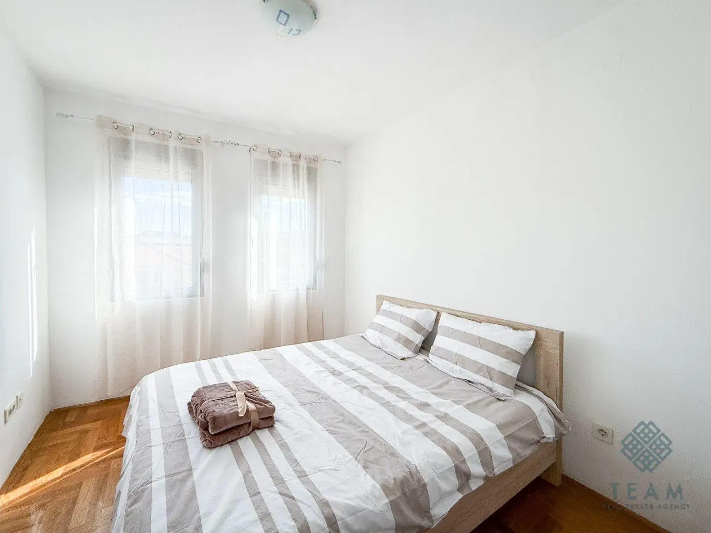 Bedroom with a double bed and windows with white curtains.