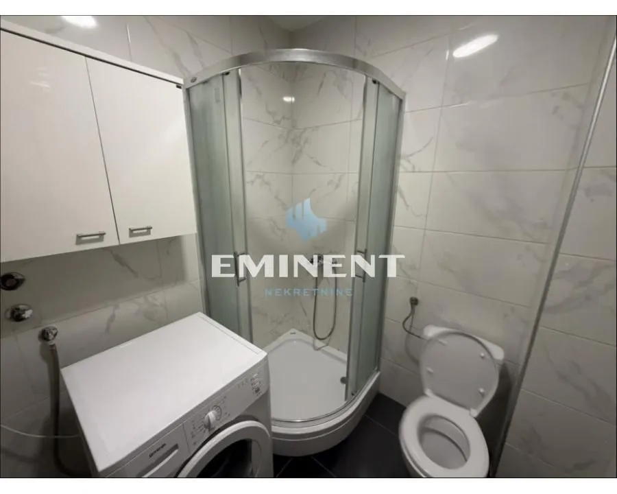 Kupatilo opremljeno tuš kabinom, WC šoljom, mašinom za veš i zidnim elementom.
