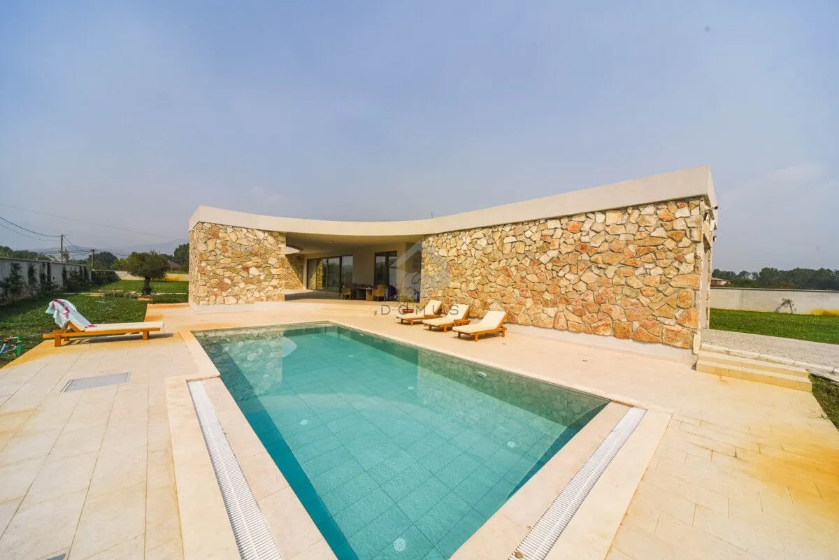 View of a modernly landscaped yard with a swimming pool and sun loungers in front of the house.