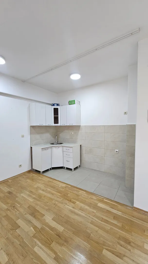 Smaller white kitchen within a room with parquet flooring.