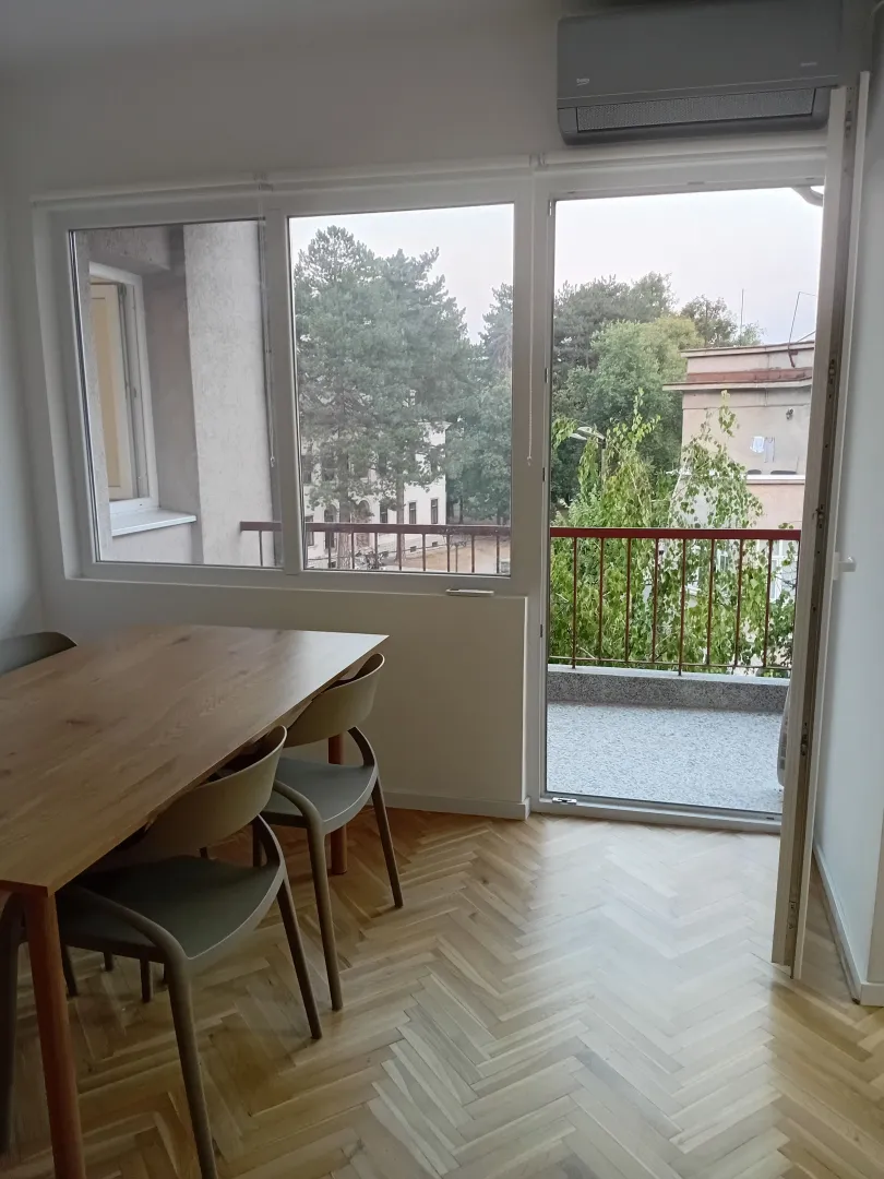 Trpezarija sa drvenim stolom i stolicama pored balkonskih vrata.