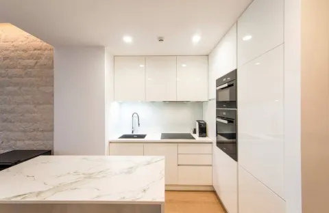 Modern white kitchen with a marble island and built-in appliances. - image 7