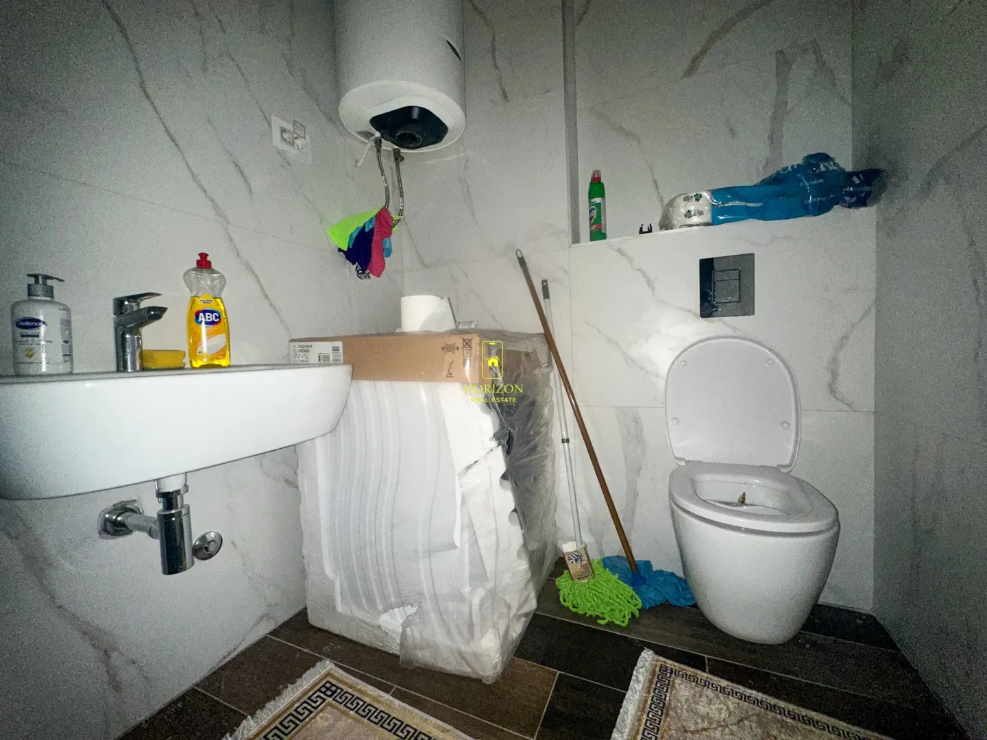 Manje kupatilo sa umivaonikom, WC šoljom i spakovanom veš mašinom.