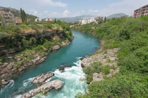 Prelijep pogled na tirkiznu rijeku i okolno zelenilo sa zgradama u daljini. - image 2