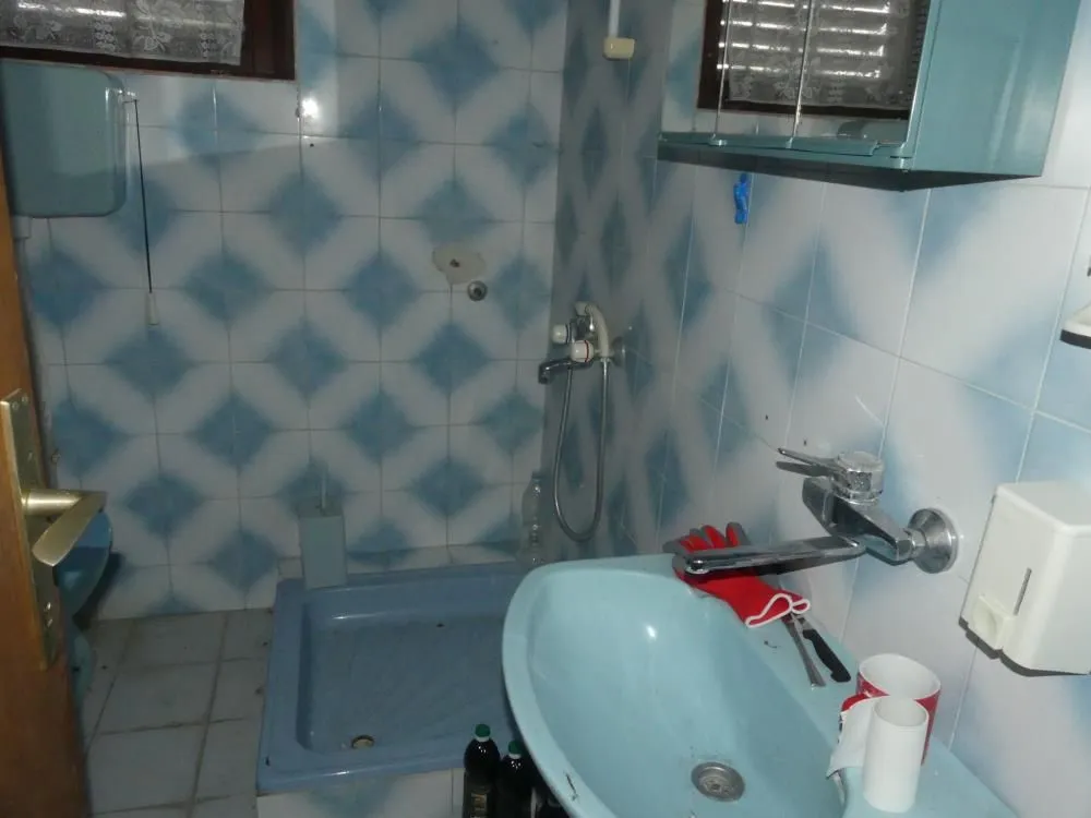 Older bathroom with blue sanitary ware and wall tiles.