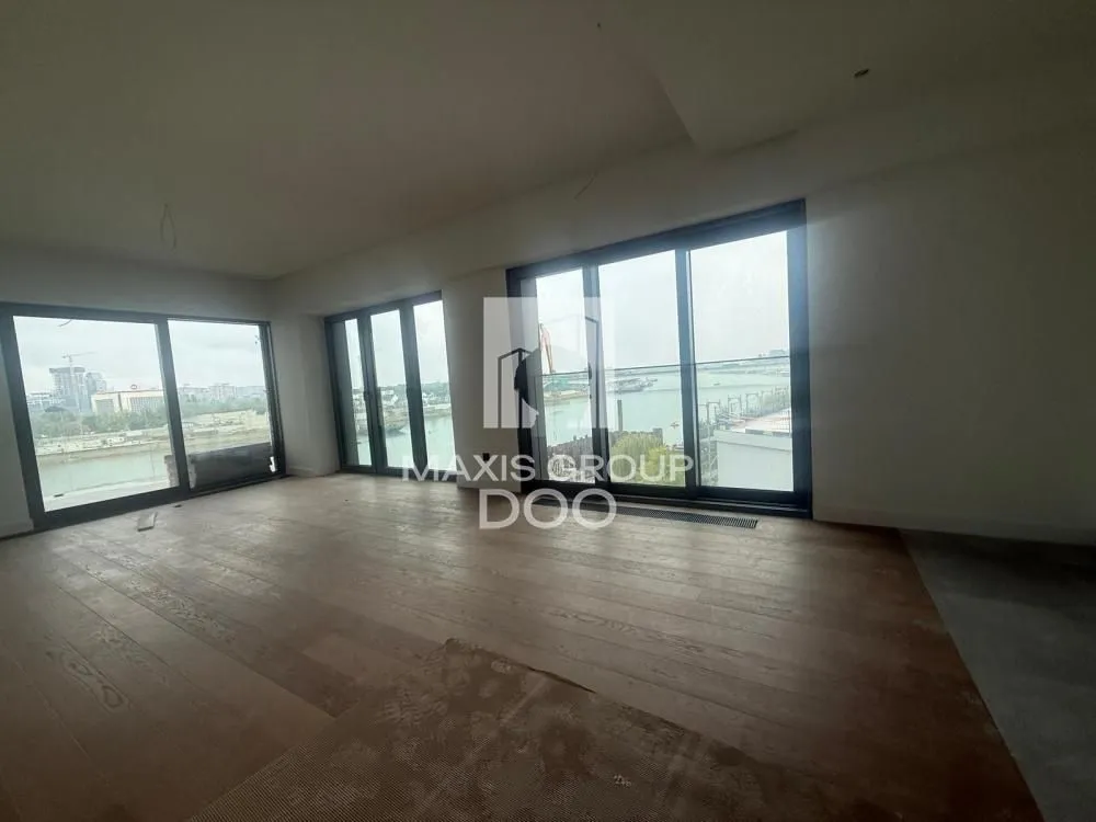 Empty room with wooden flooring and large glass surfaces overlooking the river.