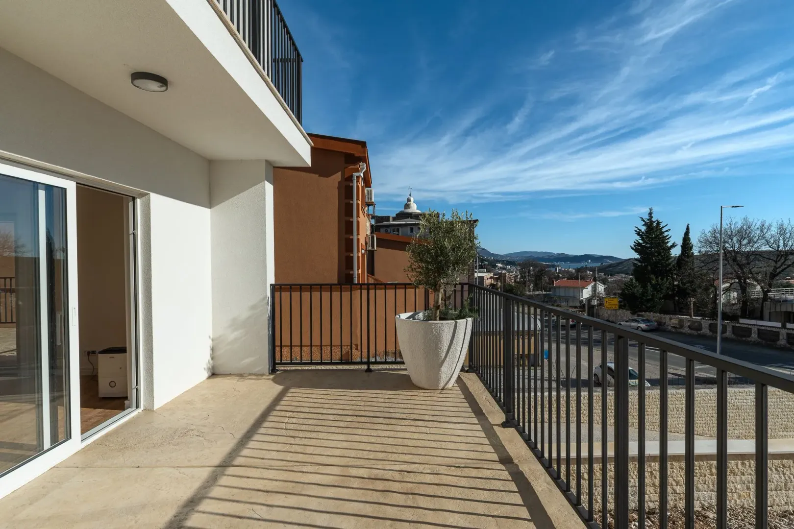 Prostrani balkon sa metalnom ogradom i pogledom na okolinu.
