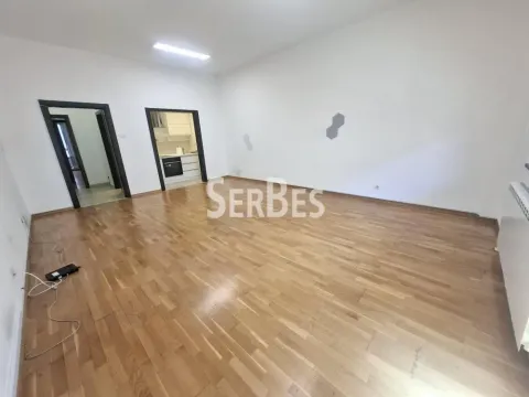 Empty room with hardwood floors and white walls, with a view of the kitchen in the background. - image 2