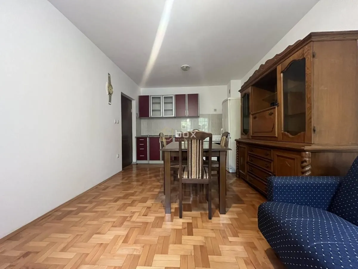 Dining area with kitchen in the background and wooden furniture.