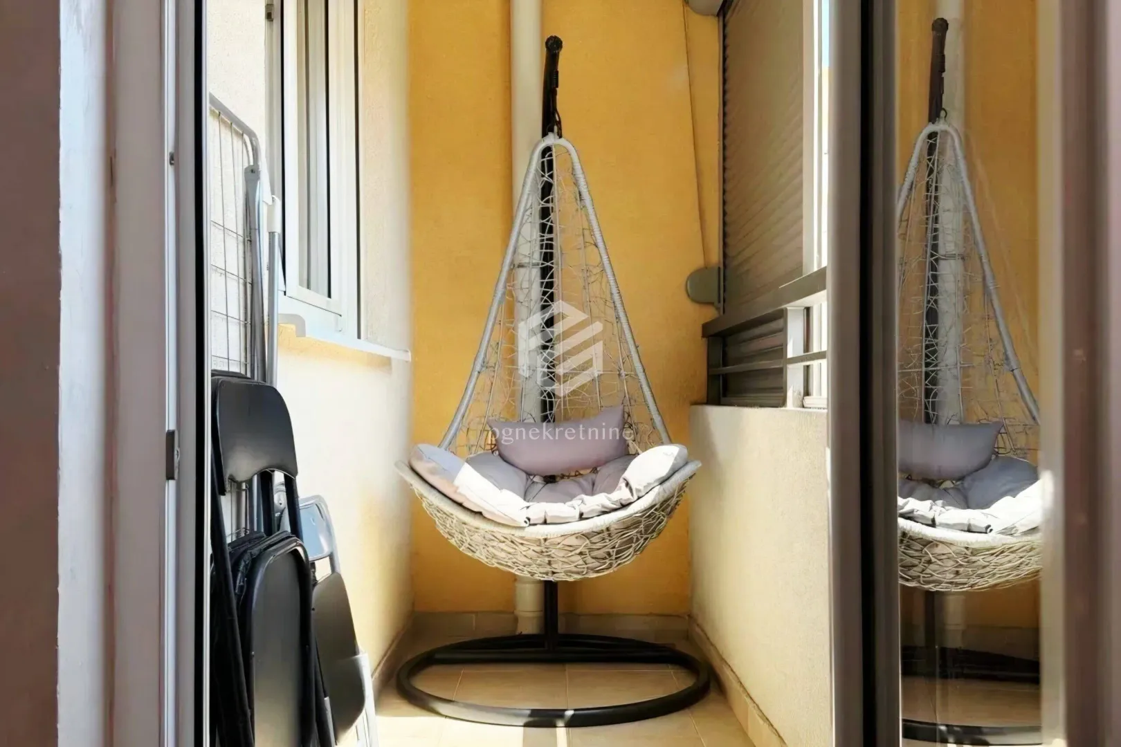 Small covered balcony with a hanging chair and folding chairs.