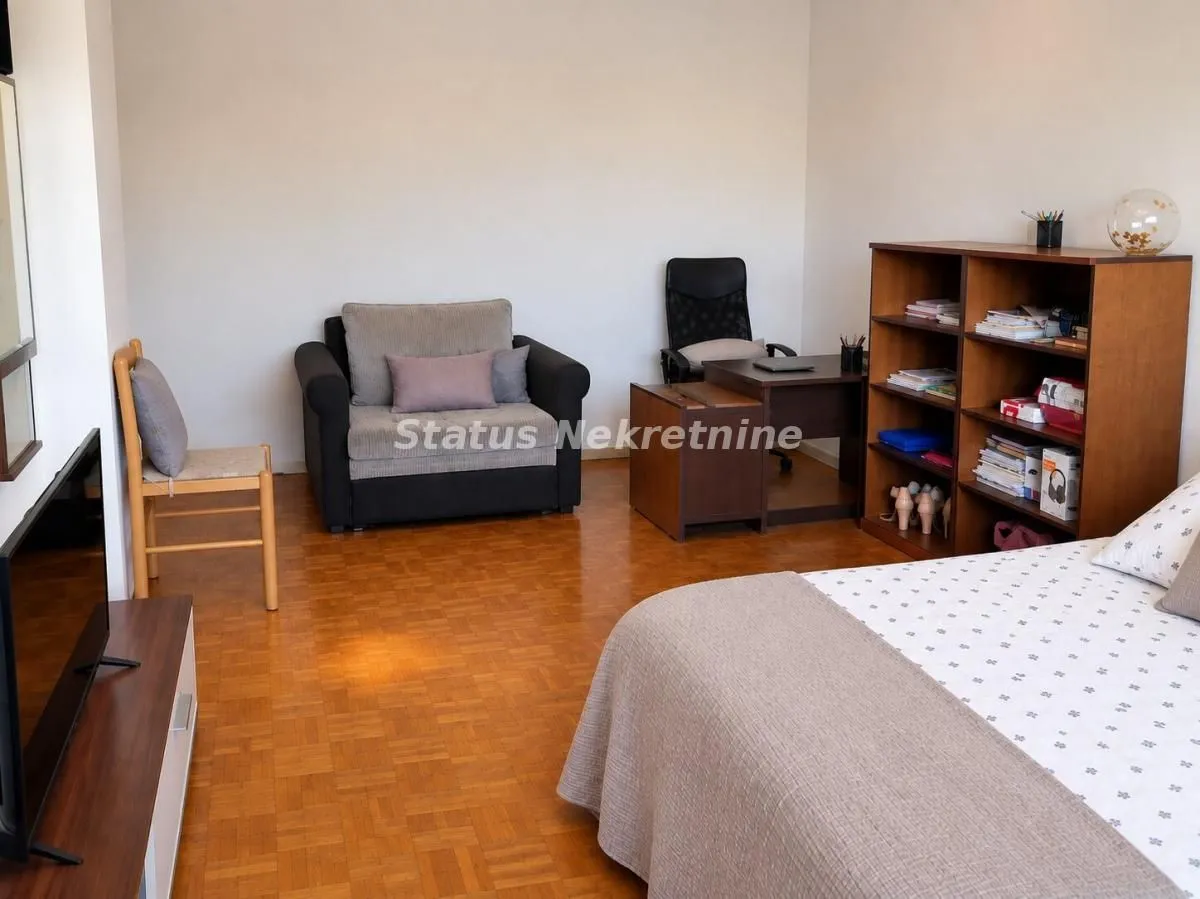 Nameštena spavaća soba sa krevetom, foteljom i radnim stolom.