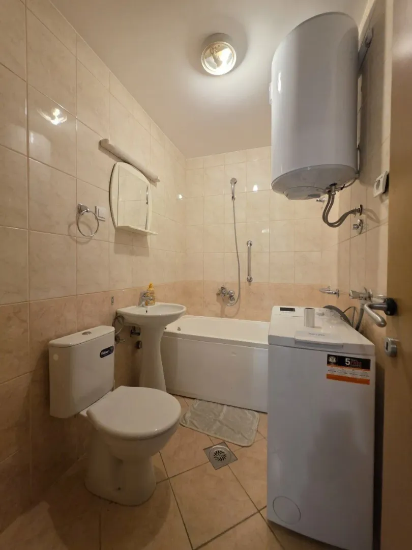 Smaller bathroom with a bathtub, washbasin, toilet, and washing machine.