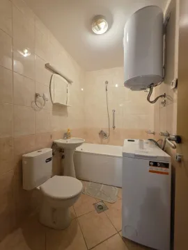 Smaller bathroom with a bathtub, washbasin, toilet, and washing machine. - image 5