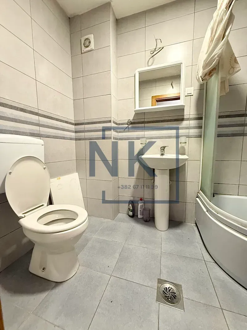Kupatilo opremljeno sanitarijama, umivaonikom, ogledalom i tuš kabinom.