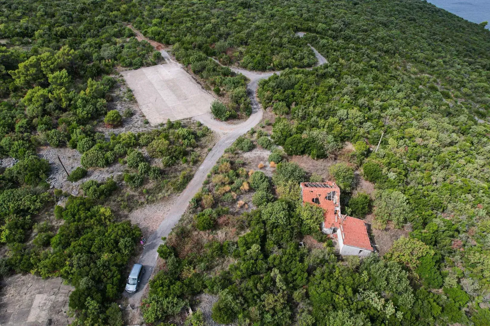 Pogled iz vazduha na plac sa ruševnim objektom i zelenilom.