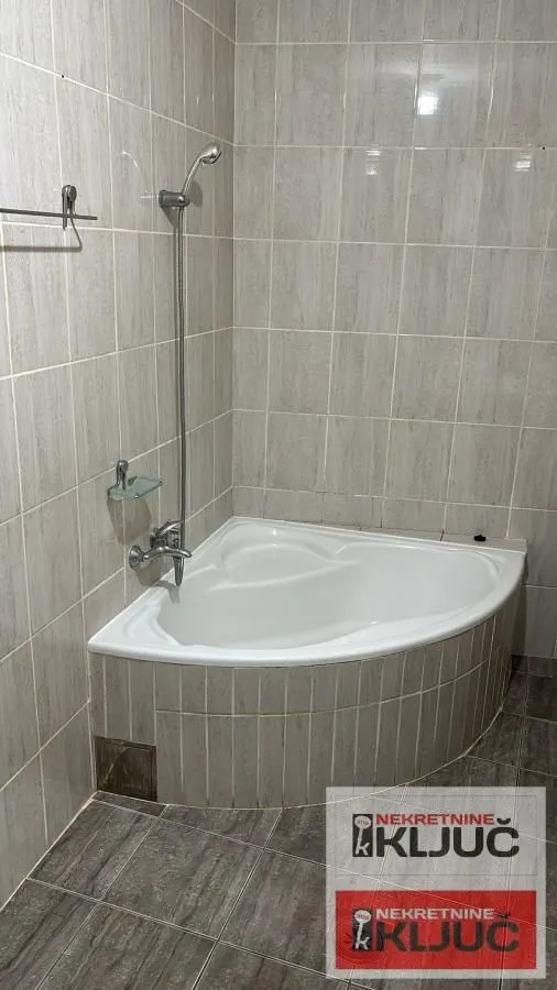 Kupatilo opremljeno ugaonom kadom i pločicama na zidovima.