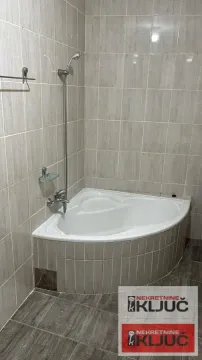 Kupatilo opremljeno ugaonom kadom i pločicama na zidovima. - image 10