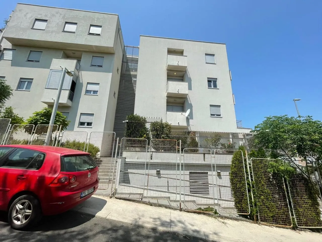 Exterior of a residential building with a fence and a parked car in the yard.