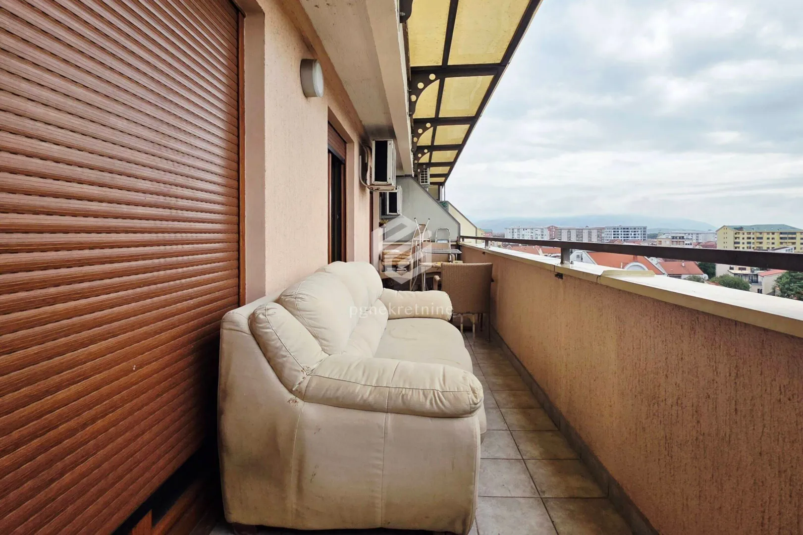 Dugačak natkriveni balkon sa garniturom za sjedenje i pogledom na naselje.