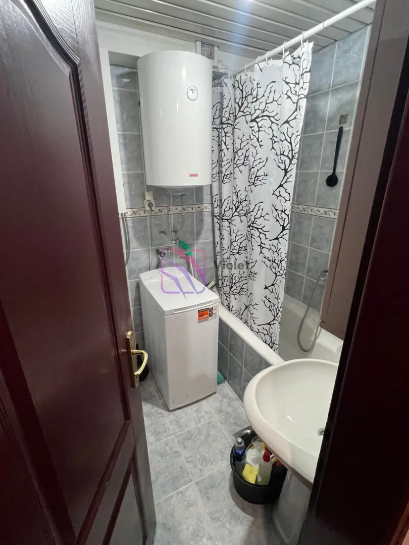 Smaller bathroom with a bathtub, washbasin, water heater, and washing machine.