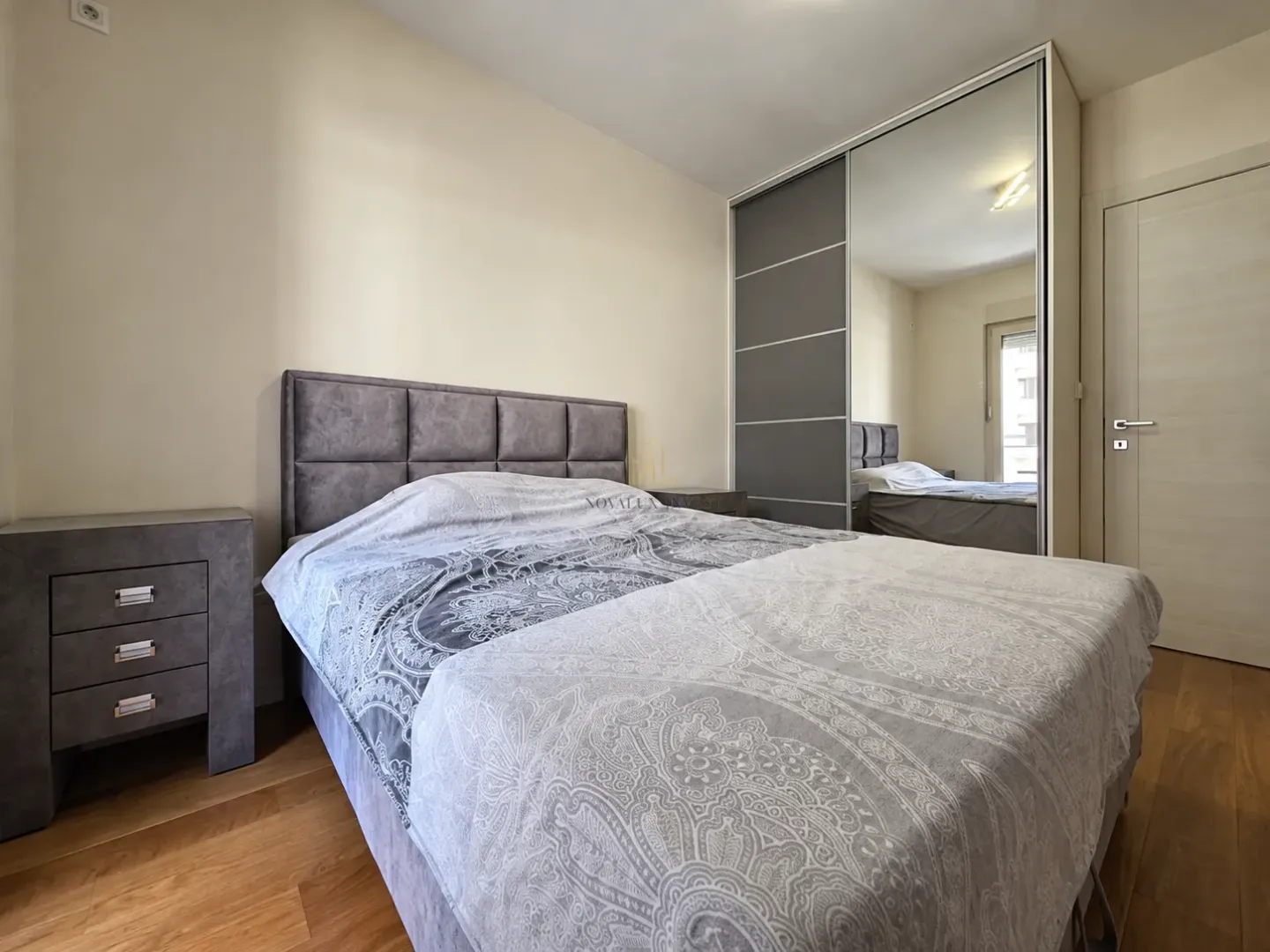 Furnished bedroom with a double bed, bedside table, and a built-in wardrobe with a mirror.