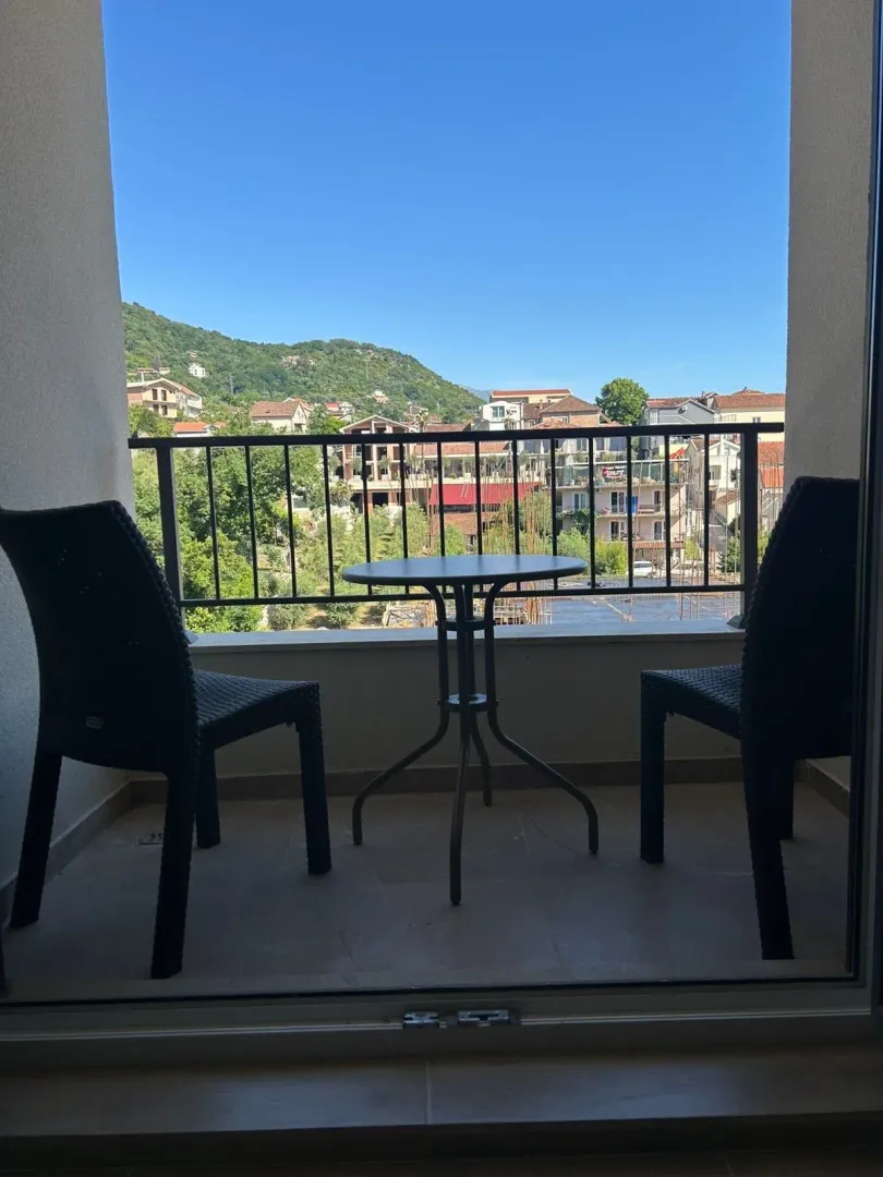 Furnished balcony with a table, chairs, and a view of the settlement and surrounding hills.