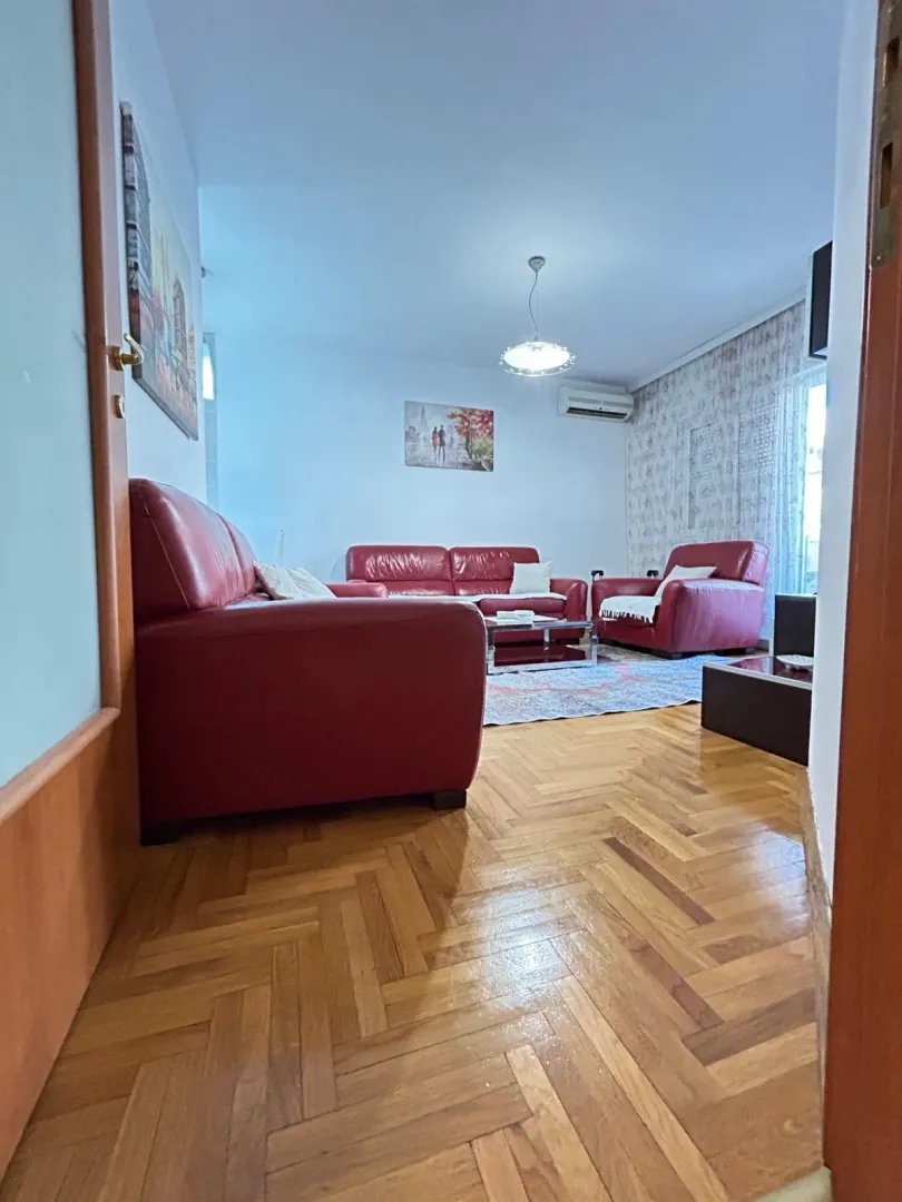 Dnevna soba sa crvenim kožnim garniturama i drvenim parketom.