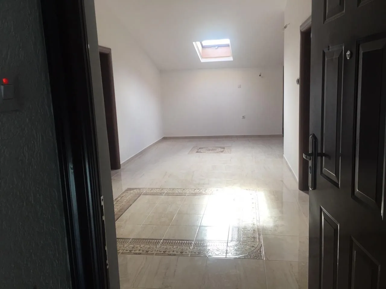 Empty attic room with a skylight and tiled floor.