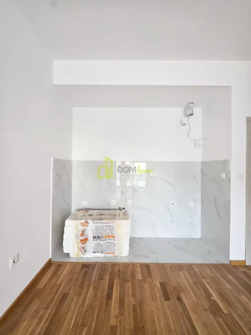 Part of a kitchen with a prepared wall covered in ceramic tiles and a wooden floor.