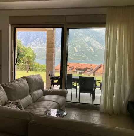 Dnevna soba sa udobnom garniturom i panoramskim pogledom na more i planine kroz staklena vrata.
