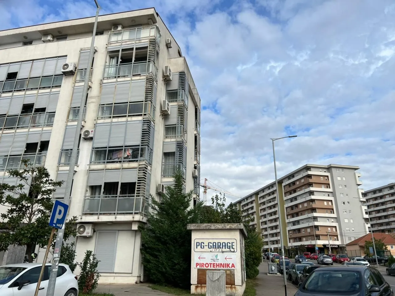 Pogled na spoljašnjost stambene zgrade i ulicu sa parkingom.