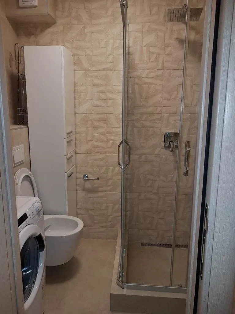 Bathroom with a shower cabin, toilet, cabinet, and washing machine.