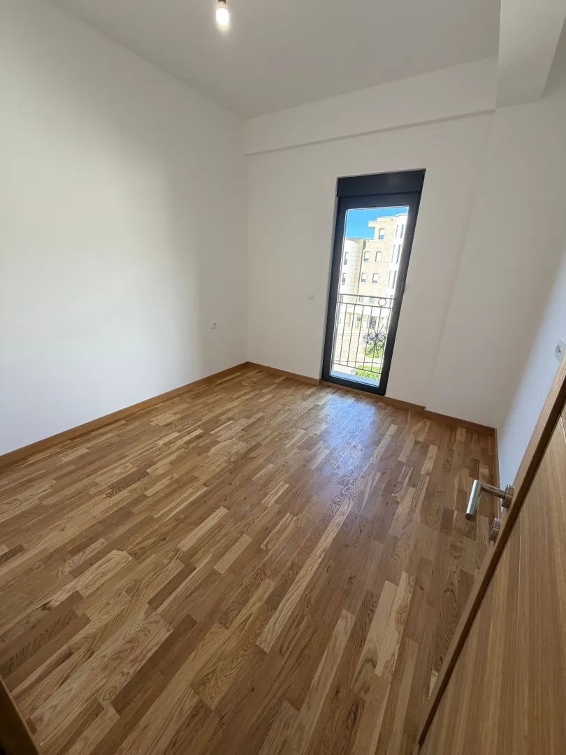 Prazna soba sa drvenim parketom i balkonskim vratima.