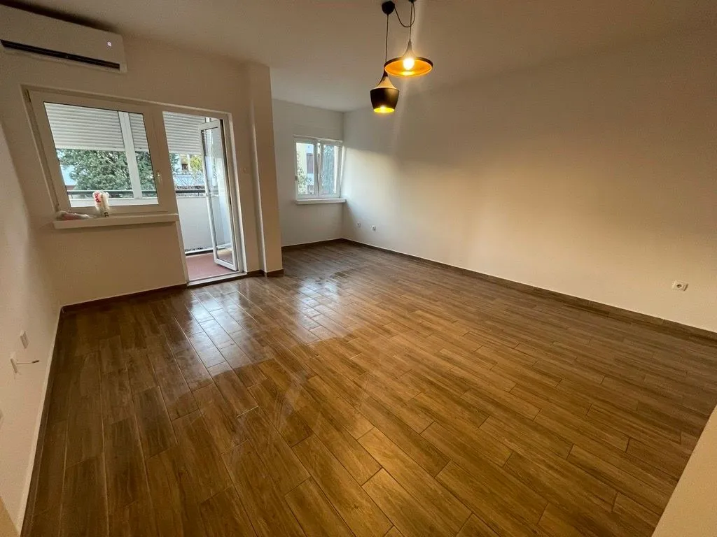 Empty living room with wood-look floor tiles and access to the terrace.