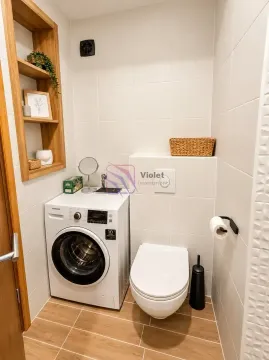 Bathroom equipped with a toilet, washing machine, and wooden shelving. - image 10