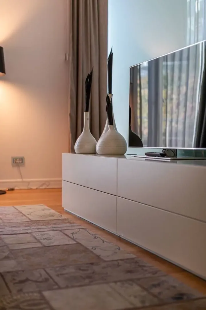 Detalj enterijera sa televizorom i ukrasnim vazama na komodi.