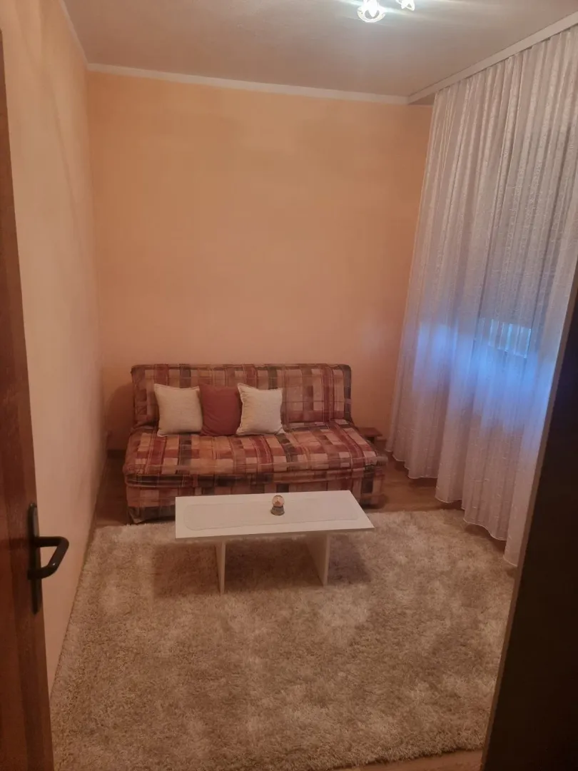 Manja dnevna soba sa garniturom za sjedenje, stočićem i prozorom sa zavjesama.