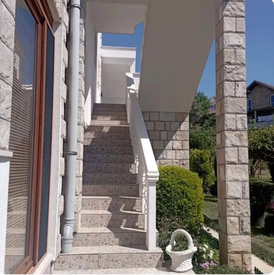 Spoljašnje stepenište kuće obloženo pločicama sa kamenim stubovima.