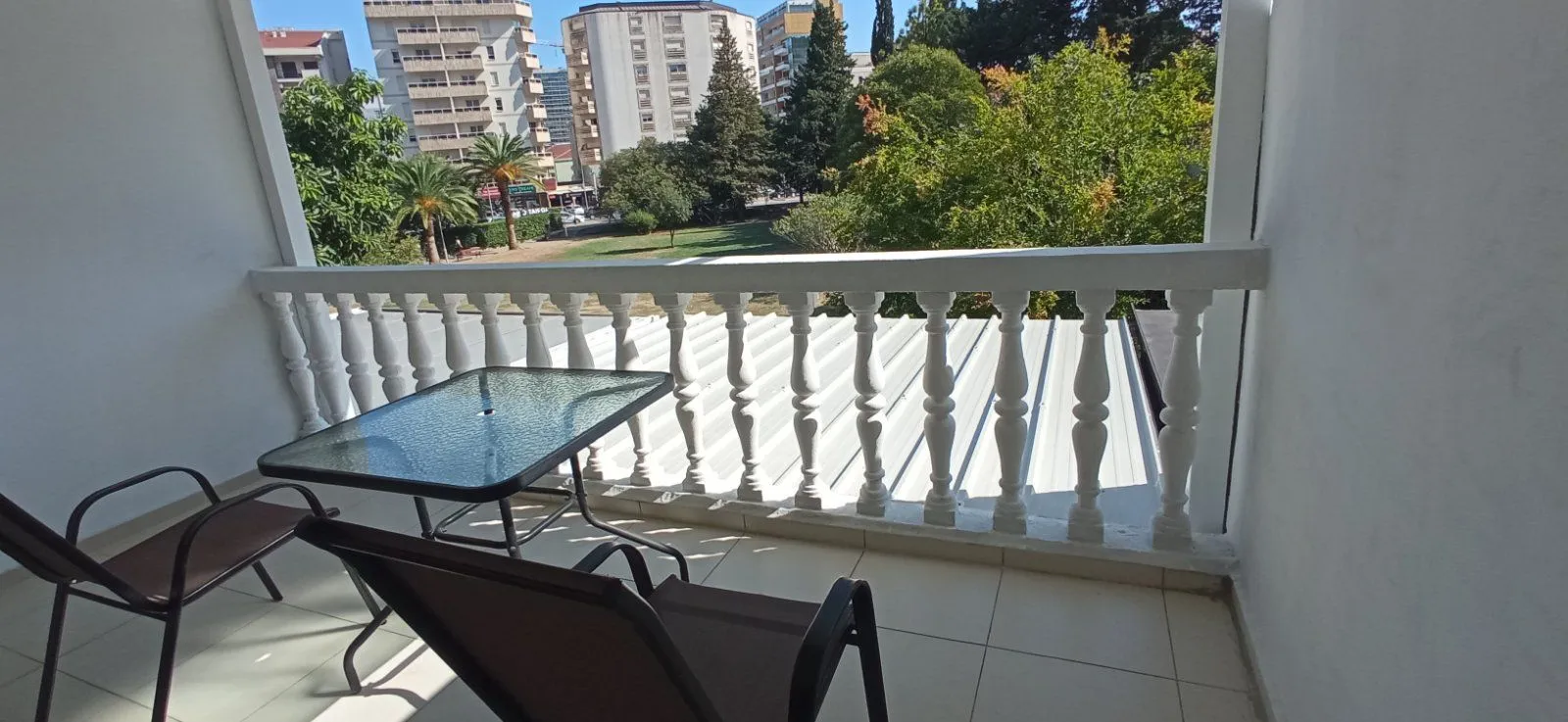 Covered balcony with outdoor seating and a view of the city and greenery.