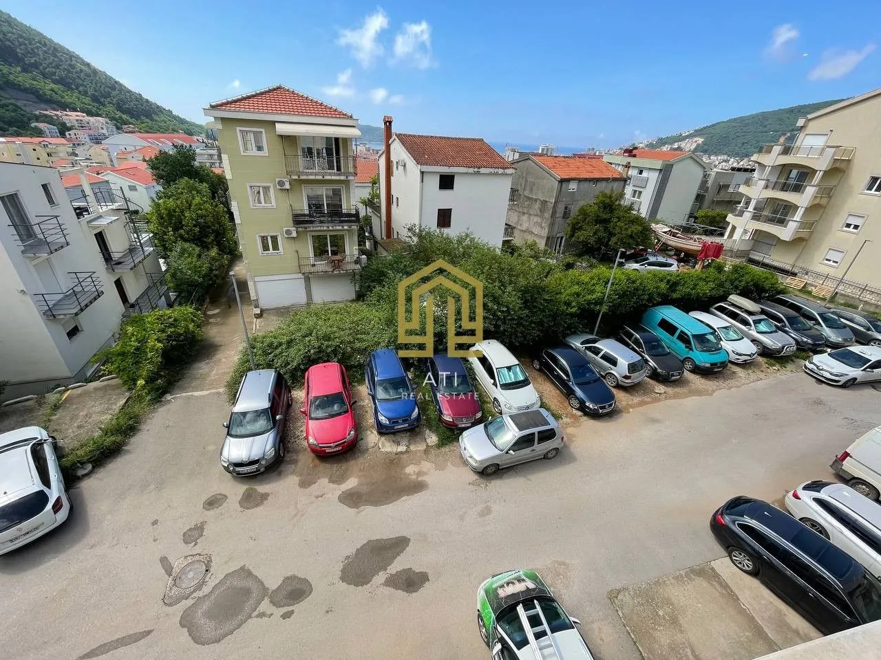 Pogled sa terase na zgradu i parking sa vozilima.