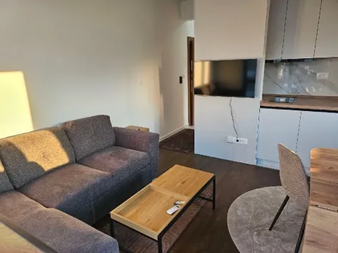Living room with a sofa, coffee table, and kitchen in the background. - image 12
