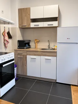 Small kitchen with white and wood-finish cabinets, a sink, and a refrigerator. - image 4