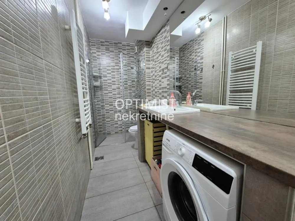 Modern bathroom with a walk-in shower, washbasin, and washing machine.