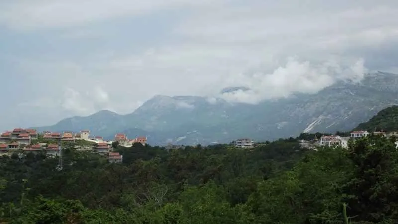 Pogled na planinski pejzaž i naselje sa zelenilom u prvom planu.