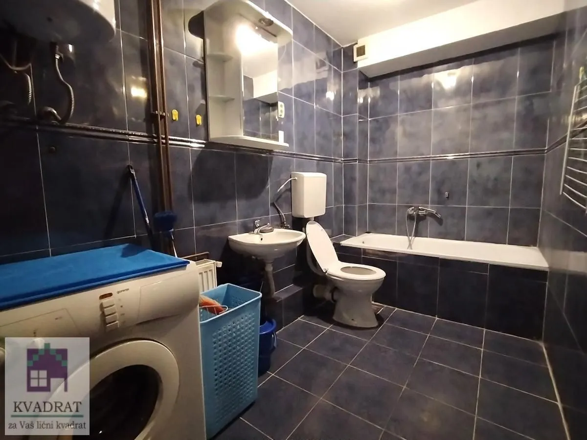 Blue tiled bathroom featuring a bathtub, washbasin, toilet, and washing machine.
