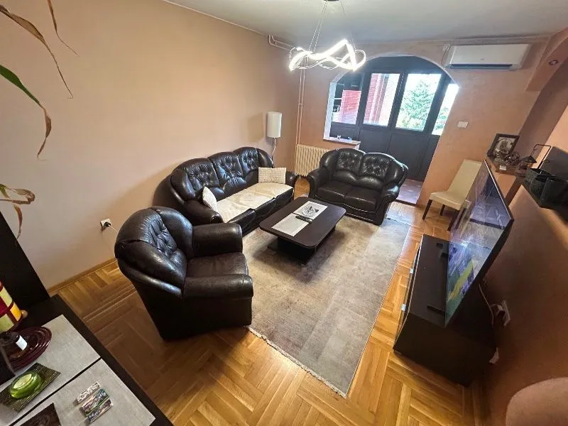 Dnevna soba sa garniturom od tamne kože, drvenim parketom i izlazom na terasu.