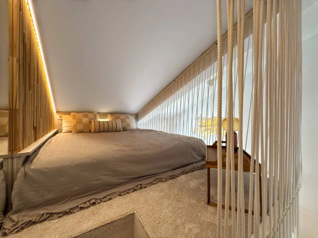 Attic bedroom with a double bed and decorative partition ropes.