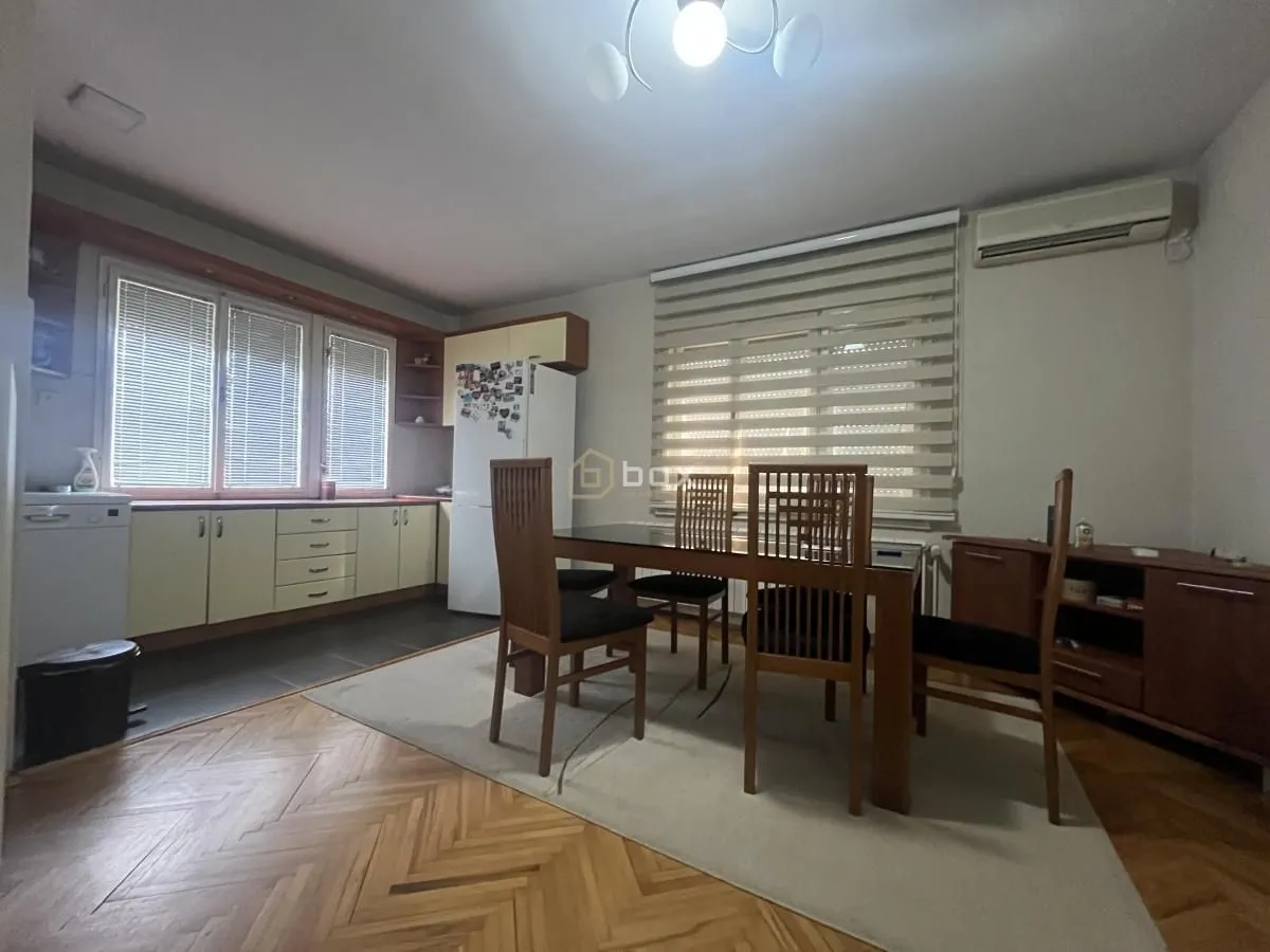 Trpezarija sa drvenim stolom i stolicama povezana sa kuhinjom.